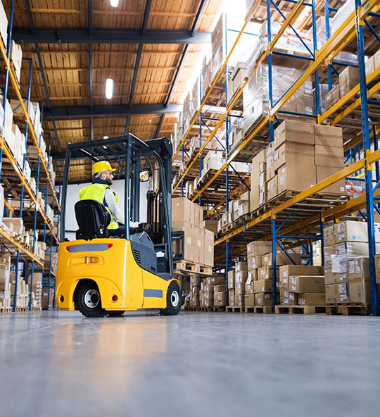 Man in a forklift in a warehouse full of boxes on tall steel shelves