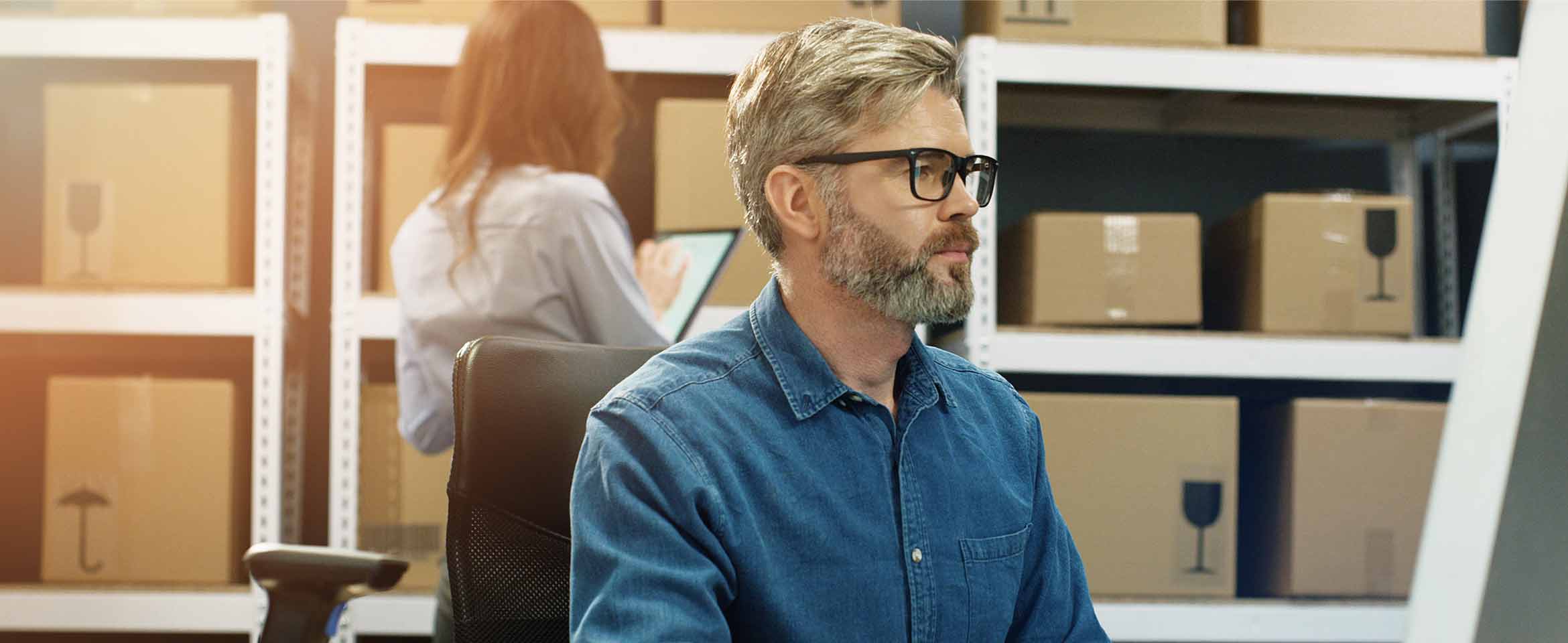 Person working at a computer in a warehouse with shelves of packaged goods, representing ecommerce fulfilment and business growth.